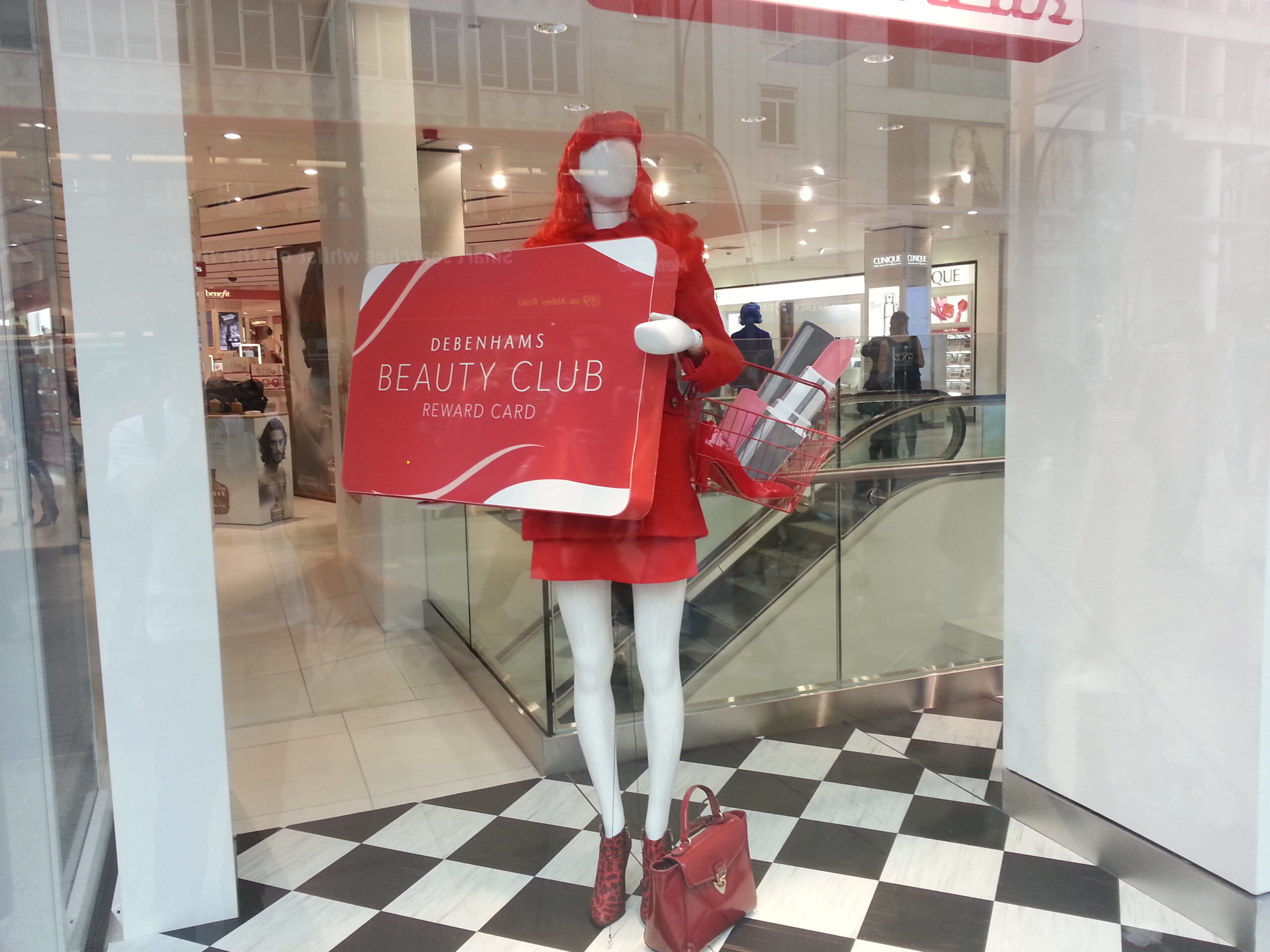 Retail display with mannequin, red outfit, promotional signage, and shopping basket filled with gift boxes