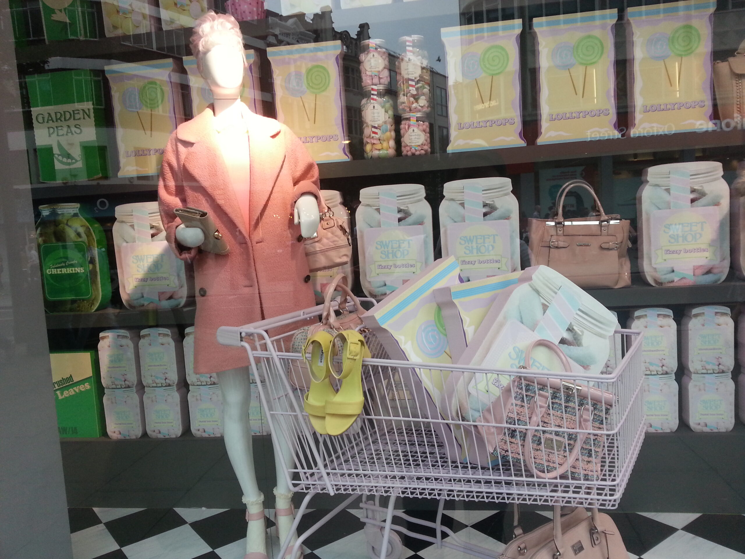 Retail window display featuring mannequin and polystyrene props including candy jars, juice cartons, and shopping cart