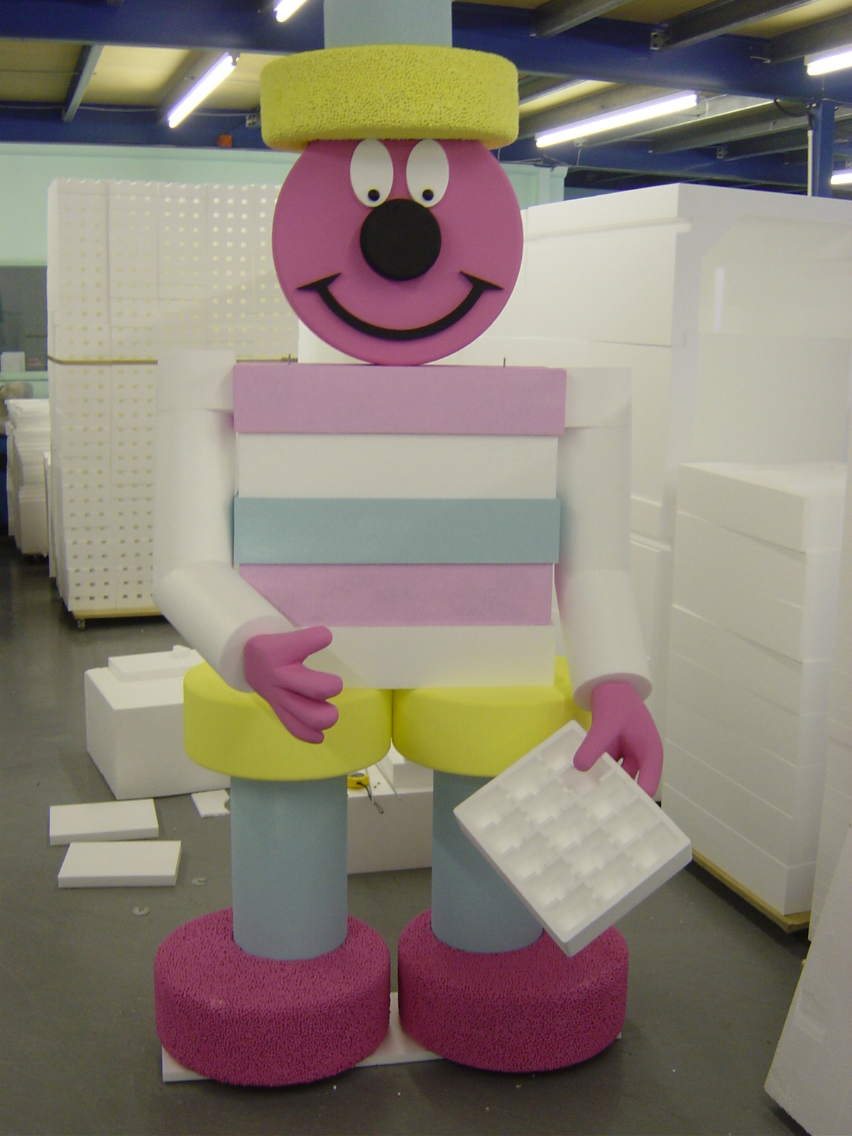 Colourful polystyrene character prop with smiling face holding foam trays in workshop