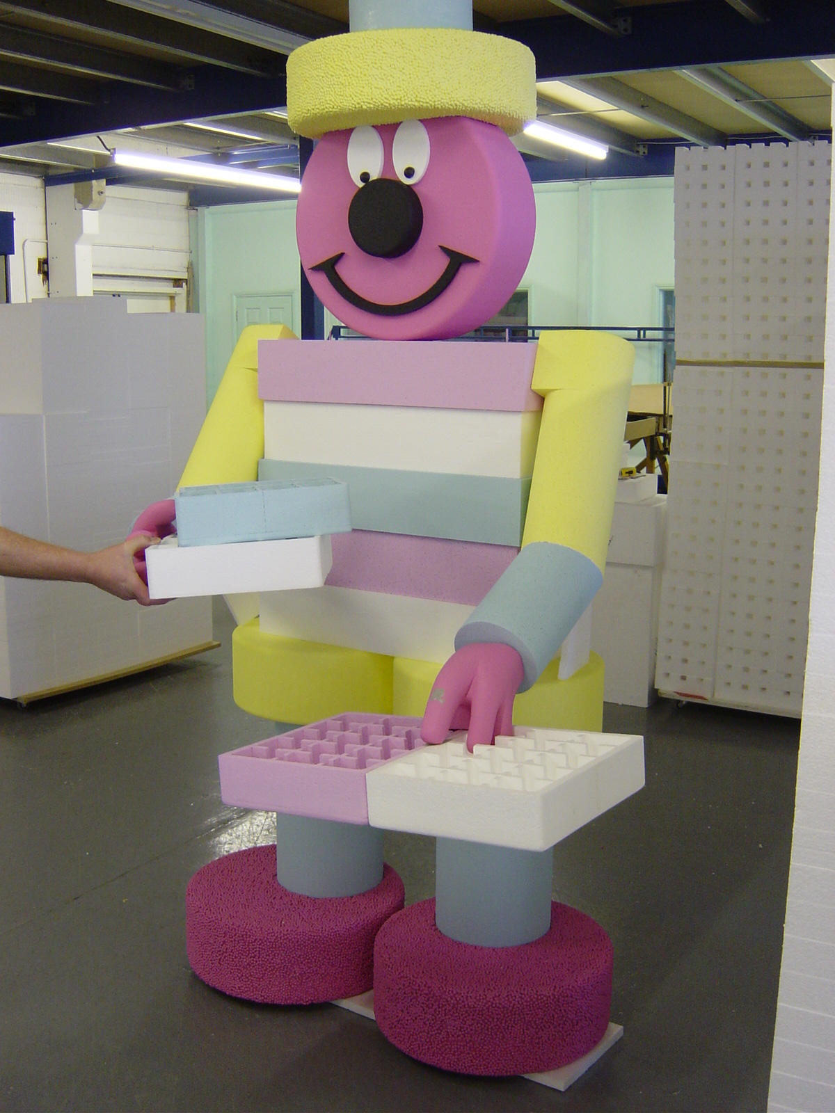 Colourful polystyrene character prop with smiling face holding foam trays in workshop