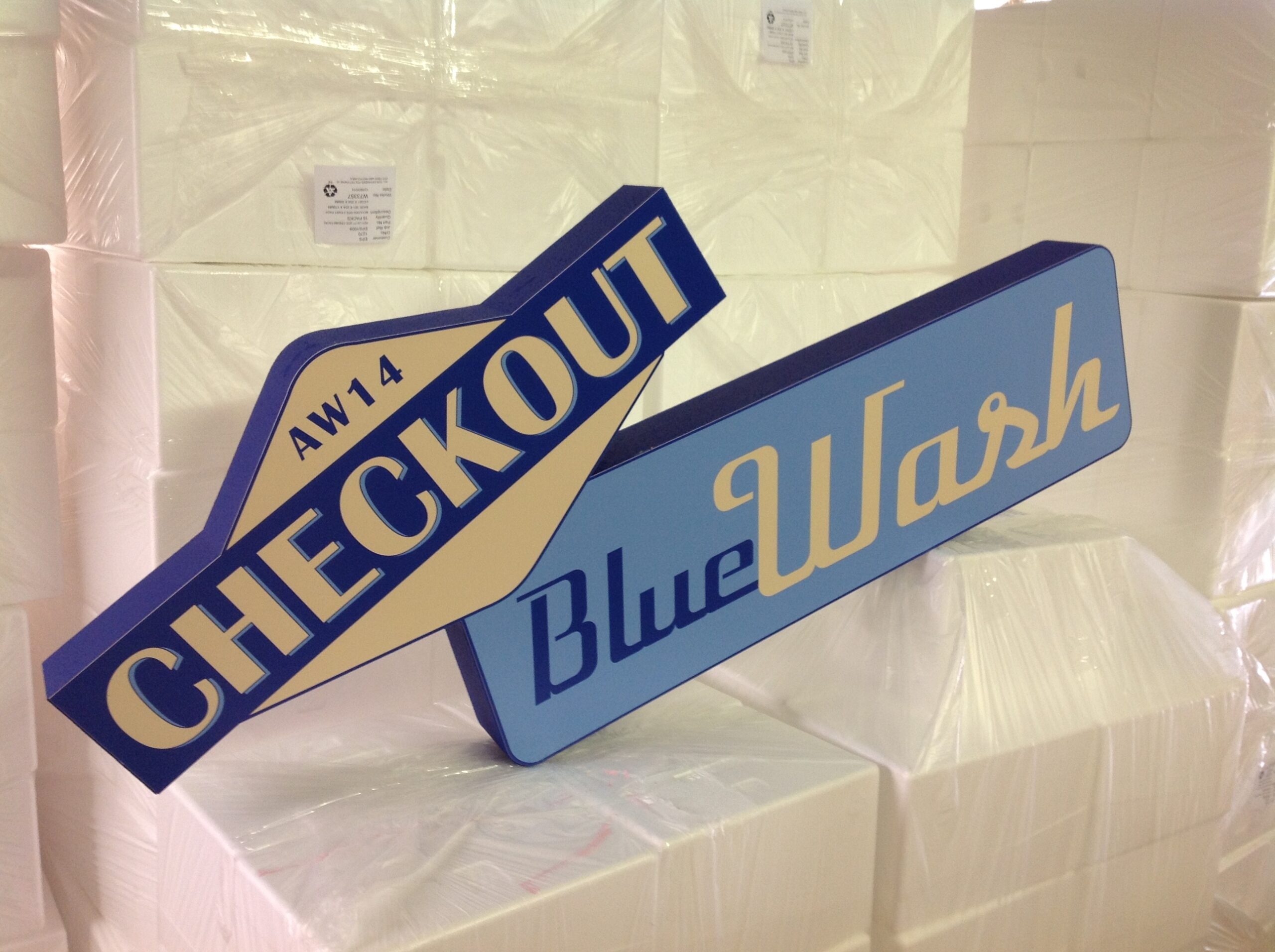Polystyrene signage props labeled AW14 CHECKOUT and BlueWash staged in workshop